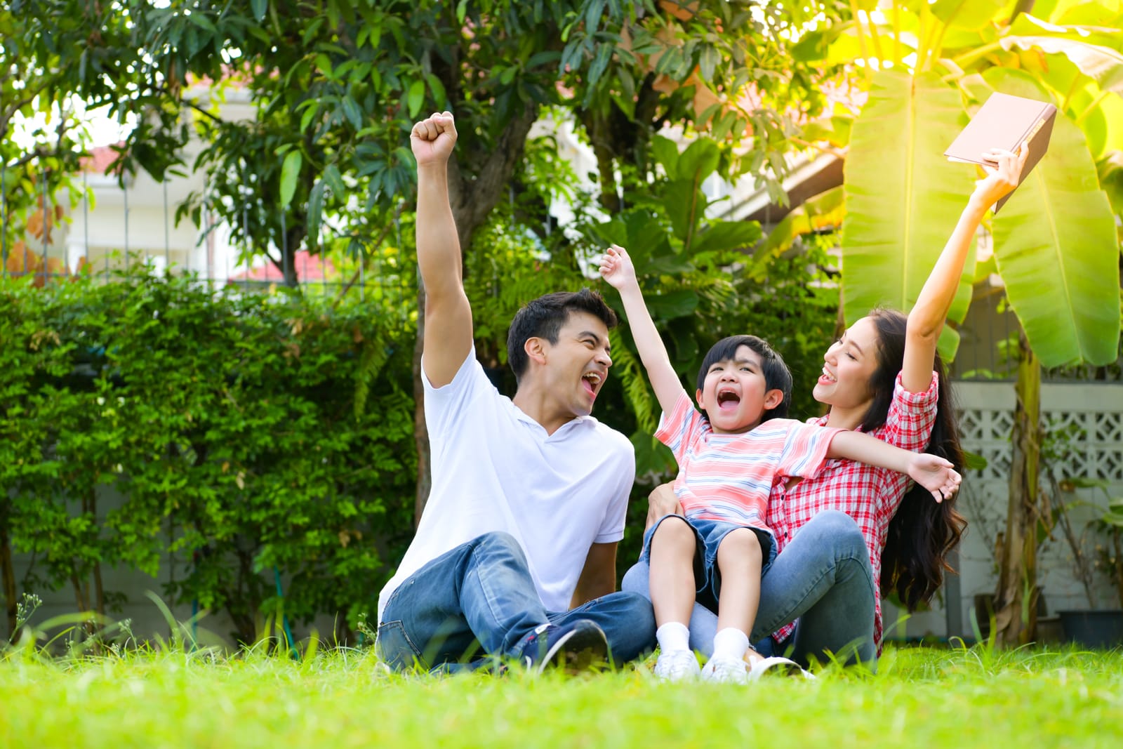 Parents and their young son cheering together on the grass in a garden